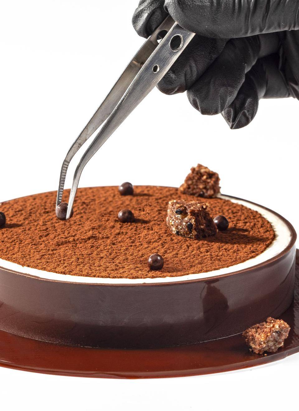 chef adicionando um crispearls com a pinça emc ima de um tiramissu com cacau em pó