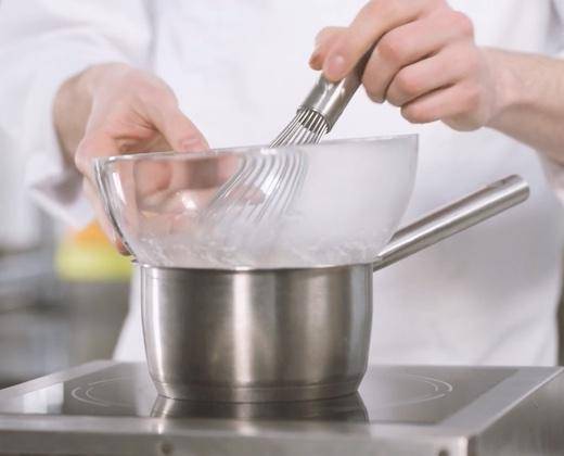 A chef gently heats egg whites over a bain marie